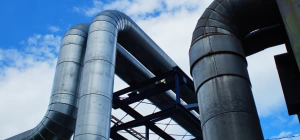 Fernwärmeleitungen in einem Blockheizkraftwerk unter blauem, leicht bewölktem Himmel