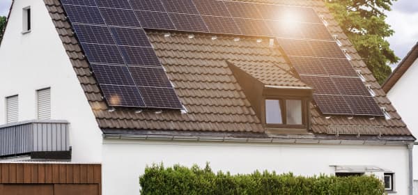 Wohnhaus mit weißer Fassade, brauner Dacheindeckung und Solarmodulen, auf die die Sonne scheint