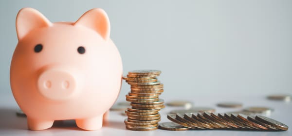 Rosa Sparschwein neben einem Münzstapel und weiteren Münzen auf weißem Untergrund