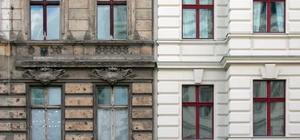 Frontansicht zweier Mehrfamilienhäuser, von denen das linke stark sanierungsbedürftig und das rechte bereits saniert ist