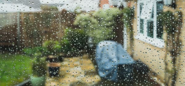 Blick aus einem Wohnhaus nach draußen aus einem Fenster, das mit Regentropfen bedeckt ist