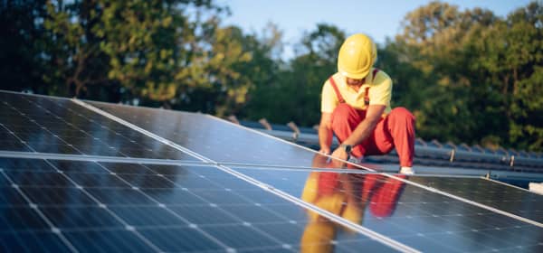 Monteur mit roter Arbeitshose und gelbem Helm montiert eine Solaranlage auf dem Dach