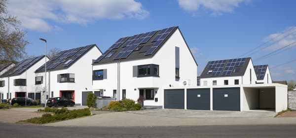 Mehrere Neubau-Einfamilienhäuser mit weißer Fassade und grauem Dach. Auf den Dächern befinden sich Solarmodule.
