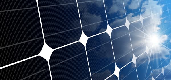 Nahansicht eines Solarmoduls, auf das die Sonne scheint, der leicht bewölkte Himmel spiegelt sich darin