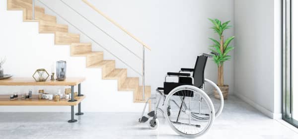Rollstuhl in hellem, modernem Raum vor einer Treppe mit Holzstufen und bodentiefen Fenstern