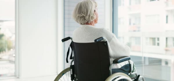 Blick auf eine Seniorin im Rollstuhl, die in einem hellen Raum aus dem Fenster blickt