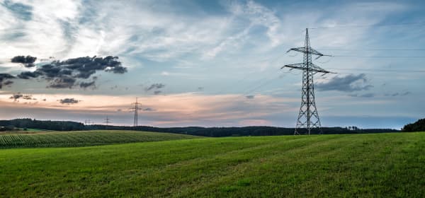 Strommasten auf grüner Wiese vor bewölktem Himmel