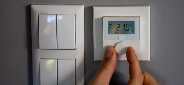 Lichtschalter und digitales Heizungsthermostat an der Wand. Eine Hand regelt die Temperatur.