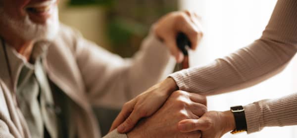 Nahaufnahme von zwei Personen, eine jüngere hält einem Senior die Hand