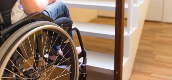 Nahaufnahme einer Person im Rollstuhl am Fuß einer Treppe von hinten