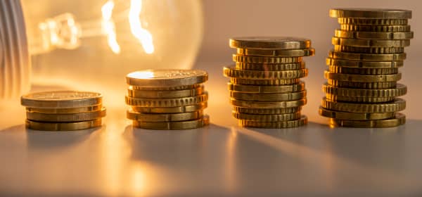 Münzstapel in unterschiedlicher Höhe vor einer leuchtenden Glühbirne