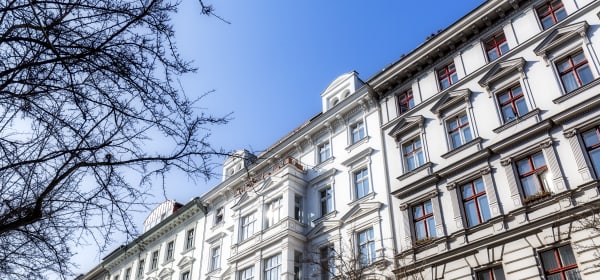Weise Fassaden von Mehrfamilienhäusern in Berlin Kreuzberg im Winter mit blätterlosen Bäumen im Vordergrund und blauem Himmel über den Dächern