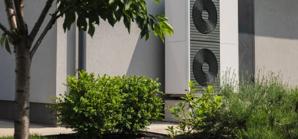 Moderne Wärmepumpen an der Fassade eines Wohnhauses mit grünem Garten