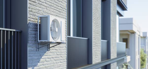 Wärmepumpe an der Fassade eines Mehrfamilienhauses zwischen zwei Balkonen