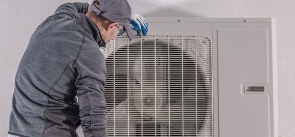 Techniker arbeitet an einer Luft-Wärmepumpe, die vor einem Haus angebracht ist