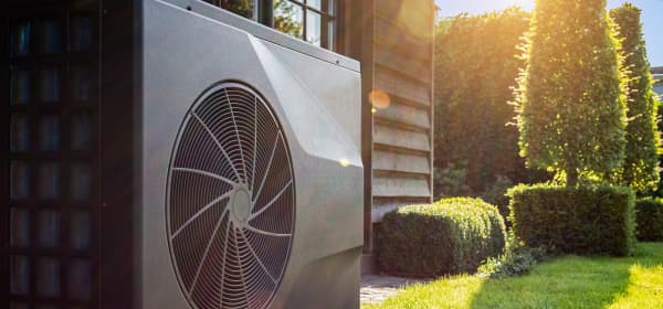 Wärmepumpe im Garten, neben Poolhaus mit Holzfassade an einem sonnigen Tag
