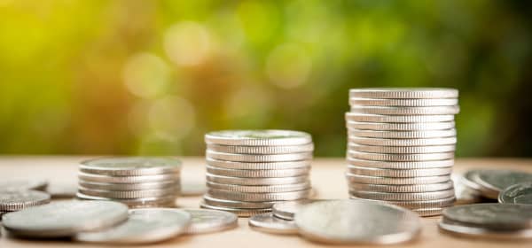 Münzen und Münzstapel in verschiedener Höhe auf braunem Untergrund vor verschwommenem, grünem Hintergrund