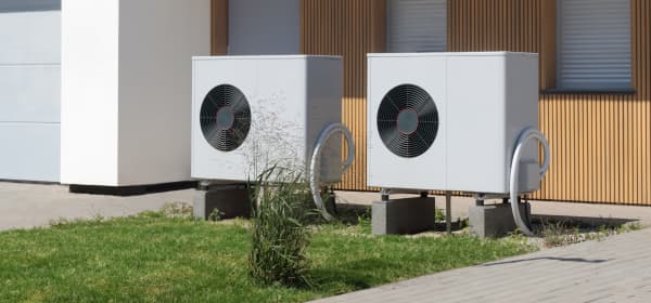 Zwei Luftwärmepumpen auf kleiner Rasenfläche vor Haus mit Holzvertäfelung an der Fassade
