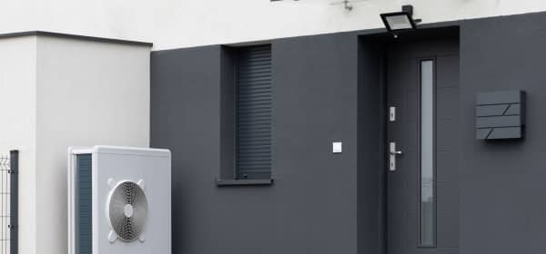 Weiße Luft-Wärmepumpe auf Sockel steht an modernem, dunklem Wohnhaus