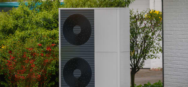 Luftwärmepumpe vor grüner Hecke an der Ecke eines Wohnhauses
