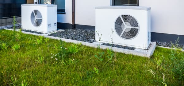 Zwei weiße Wärmepumpen vor weißer Fassade eines Wohngebäudes, davor grünes Gras