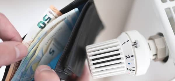 Nahaufnahme einer Geldbörse mit Bargeld neben Thermostat am Heizkörper