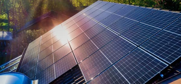 Schrägansicht eines mit Solarmodulen bedeckten Hausdachs. Die Sonne scheint durch bewölkten Himmel auf die Module