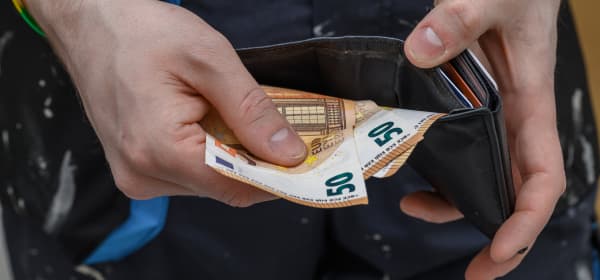 Ein Handwerker hält Geld und ein Portemonnaie in den Händen.