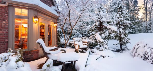 Schneebedeckter Garten und Terrasse, Blick in einen erleuchtetes Wohnzimmer eines Einfamilienhauses