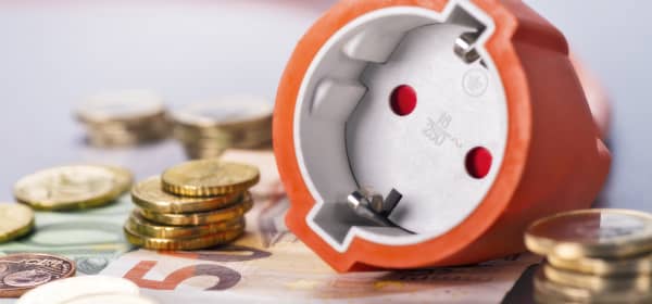 Steckdose mit orangenem Kabel liegt auf Euroscheinen und neben Münzen