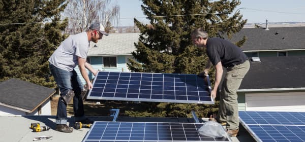 Zwei Arbeiter, die Sonnenkollektoren auf dem Dach eines Wohnhauses installieren.