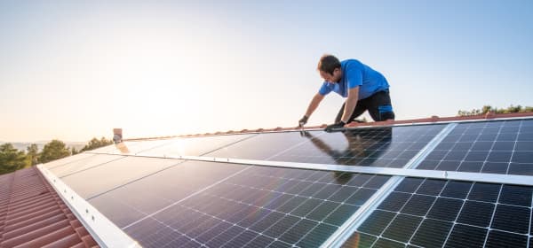 Handwerker installiert Solarmodule auf einem Schrägdach mit Ziegeln bei strahlendem Sonnenschein