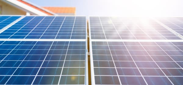 Nahaufnahme von blauen Solarmodulen mit einem klaren Rastermuster, beleuchtet von hellem Sonnenlicht. Die Module gehören zu einer Solaranlage auf einem Wohnhaus und erzeugen erneuerbare Energie zur nachhaltigen Stromversorgung.