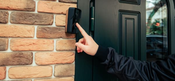 Dunkel gekleidete Person klingelt an der schwarzen Haustür eines Wohnhauses