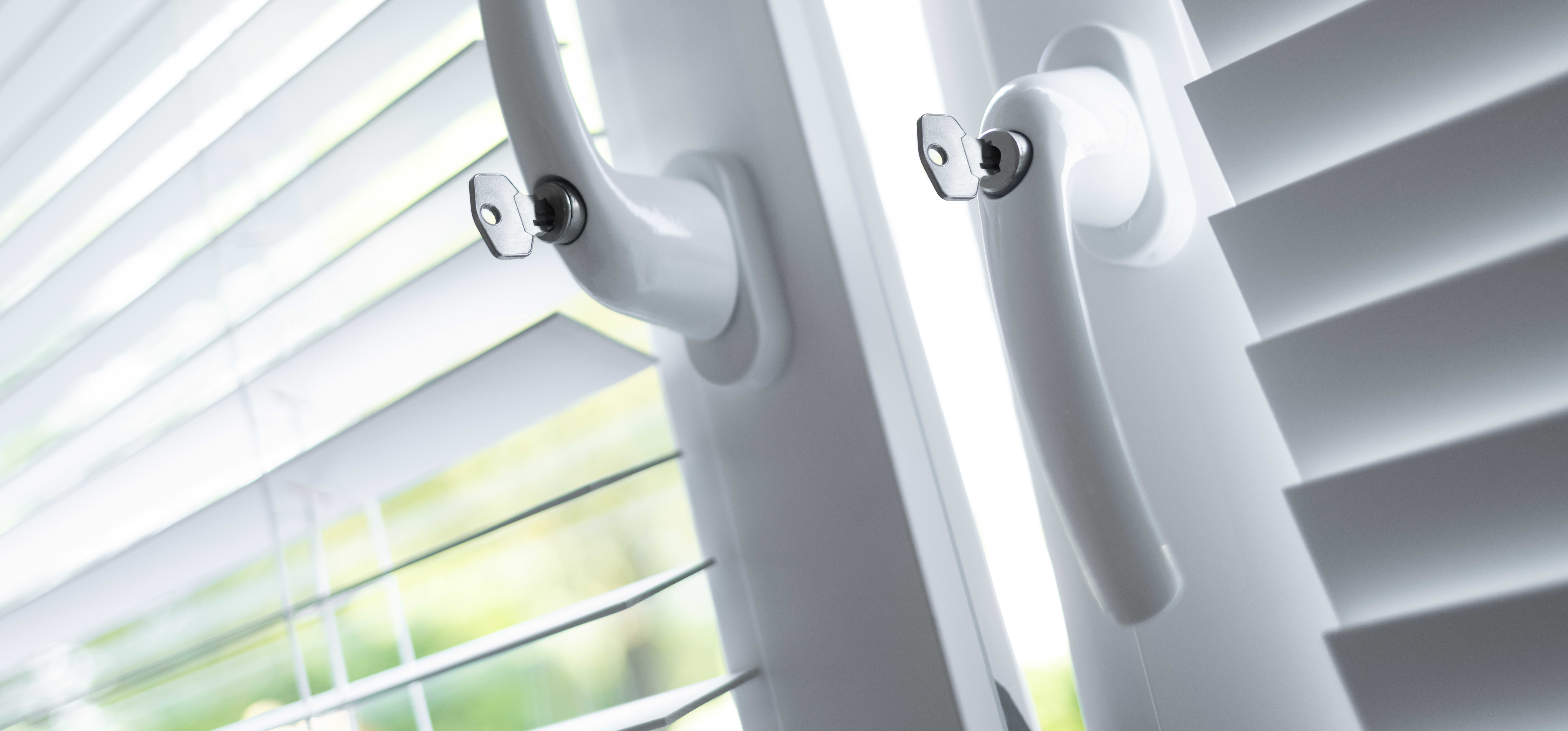 Zwei Fenster mit weißen Rollos und Sicherheitsgriffen, davon ist das linke gekippt