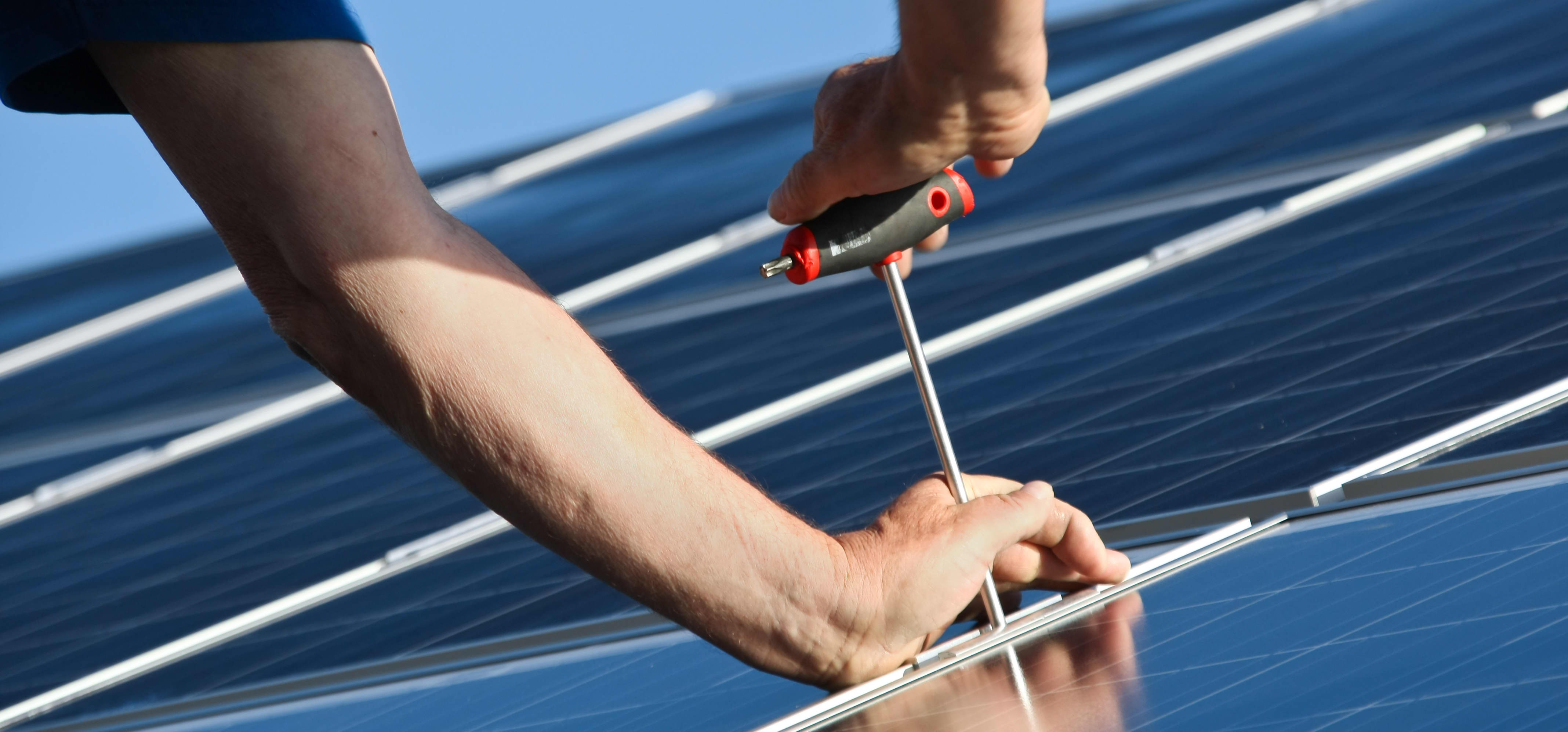Zwei Hände montieren Solarmodule auf einem Dach
