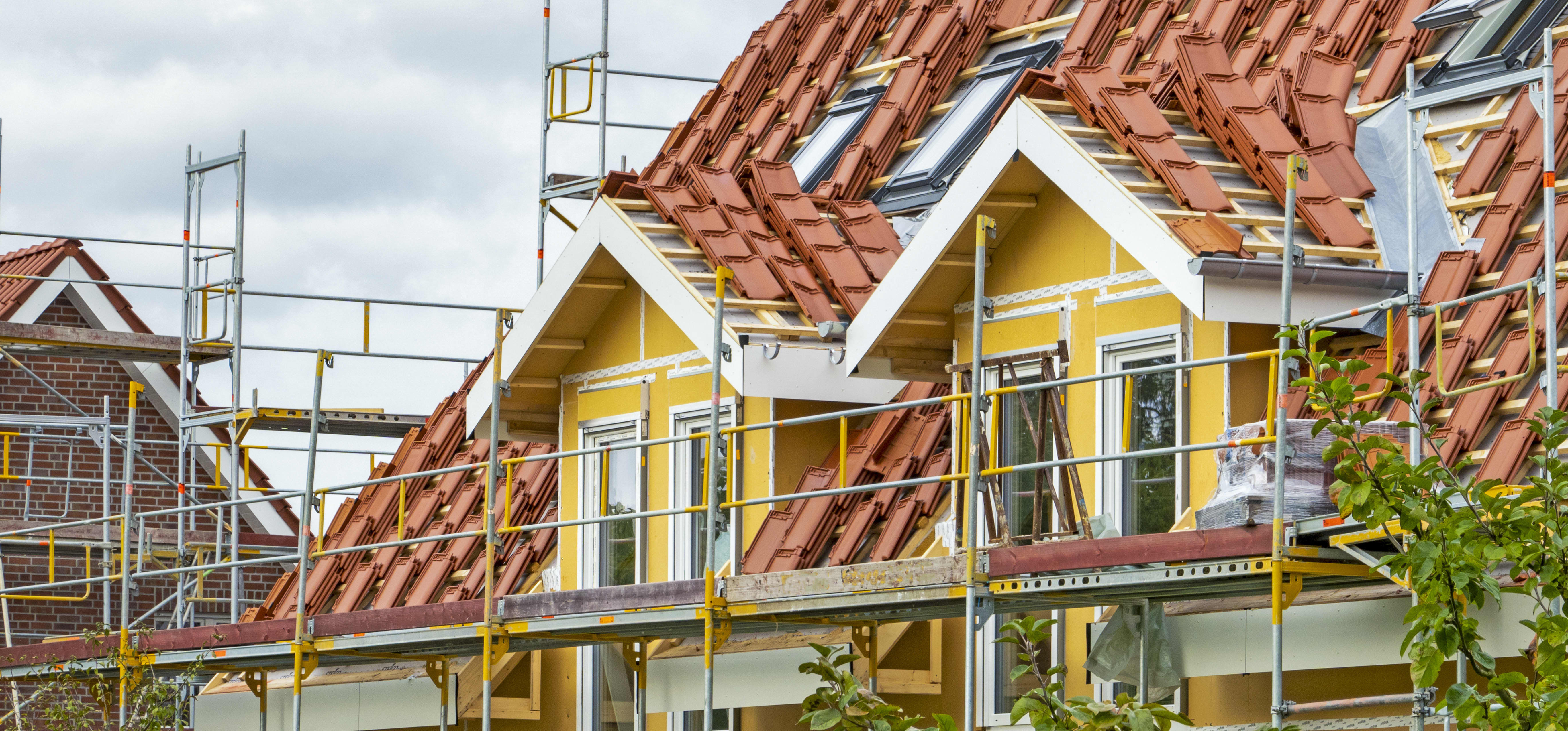 Gerüst an Wohnhaus mit gelber Fassade, dessen Dach neu gedeckt werden soll