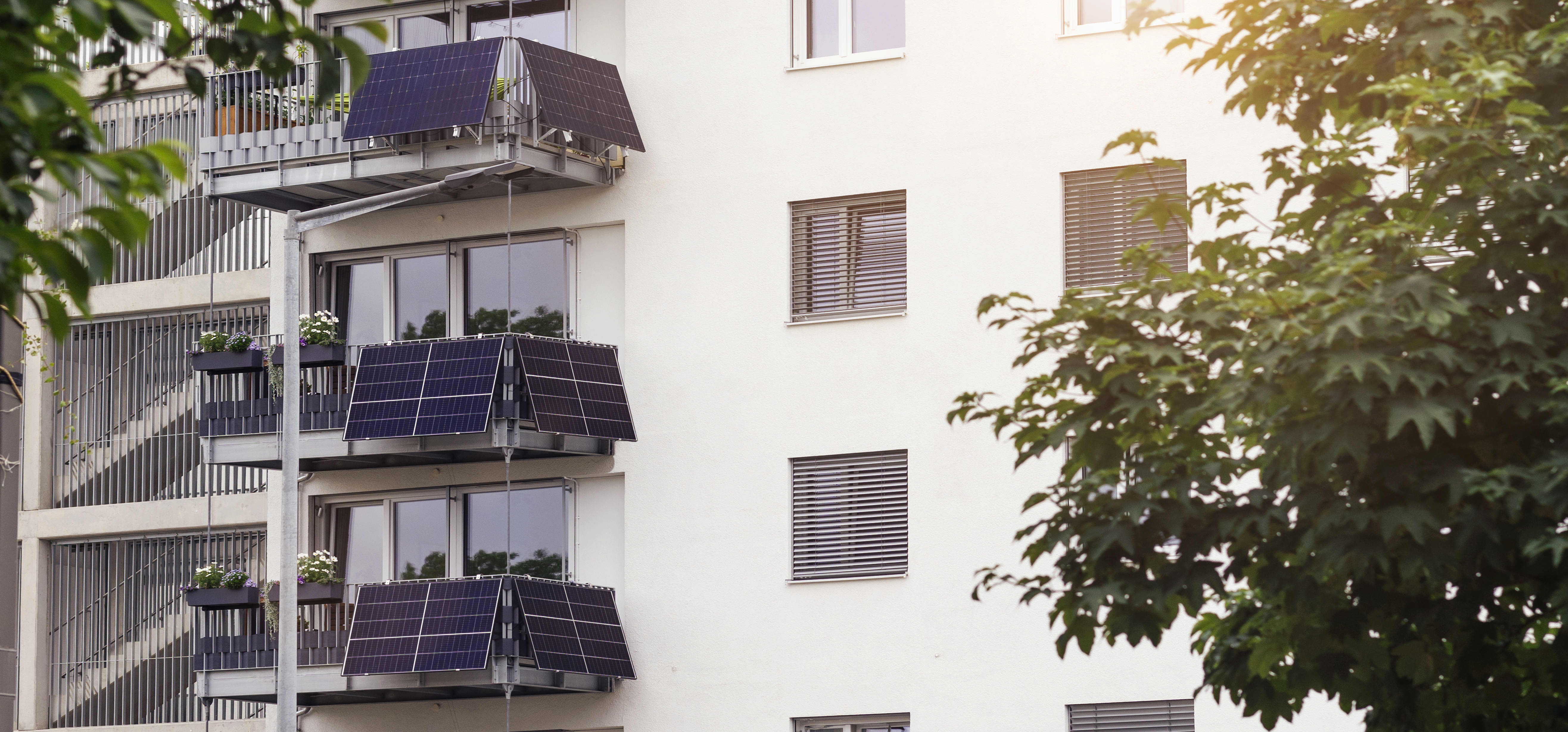 Mehrfamilienhaus mit heller Fassade und Balkonen, an denen jeweils mehrere Solarmodule installiert sind