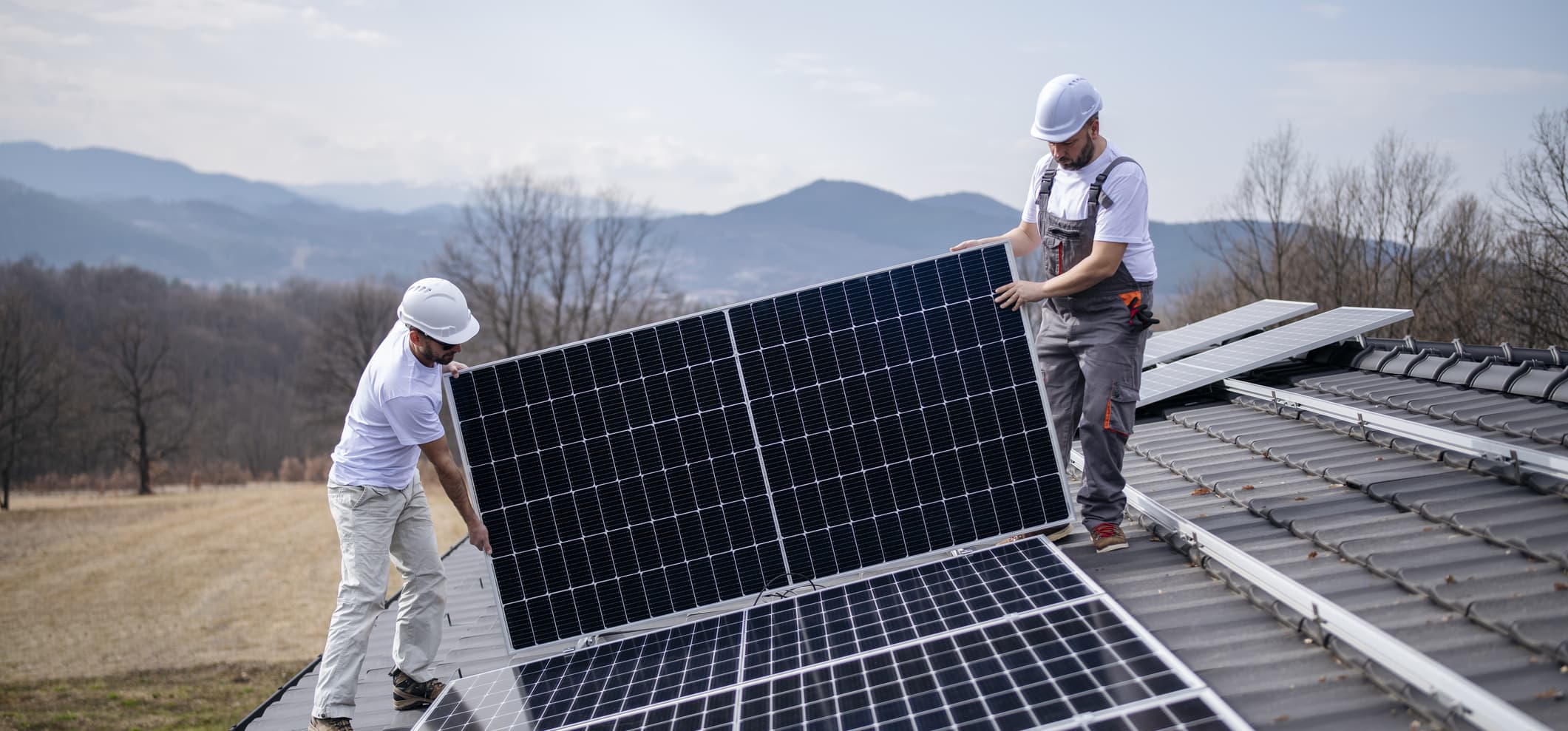 Zwei Installateure montieren ein Solarmodul auf ein Hausdach.