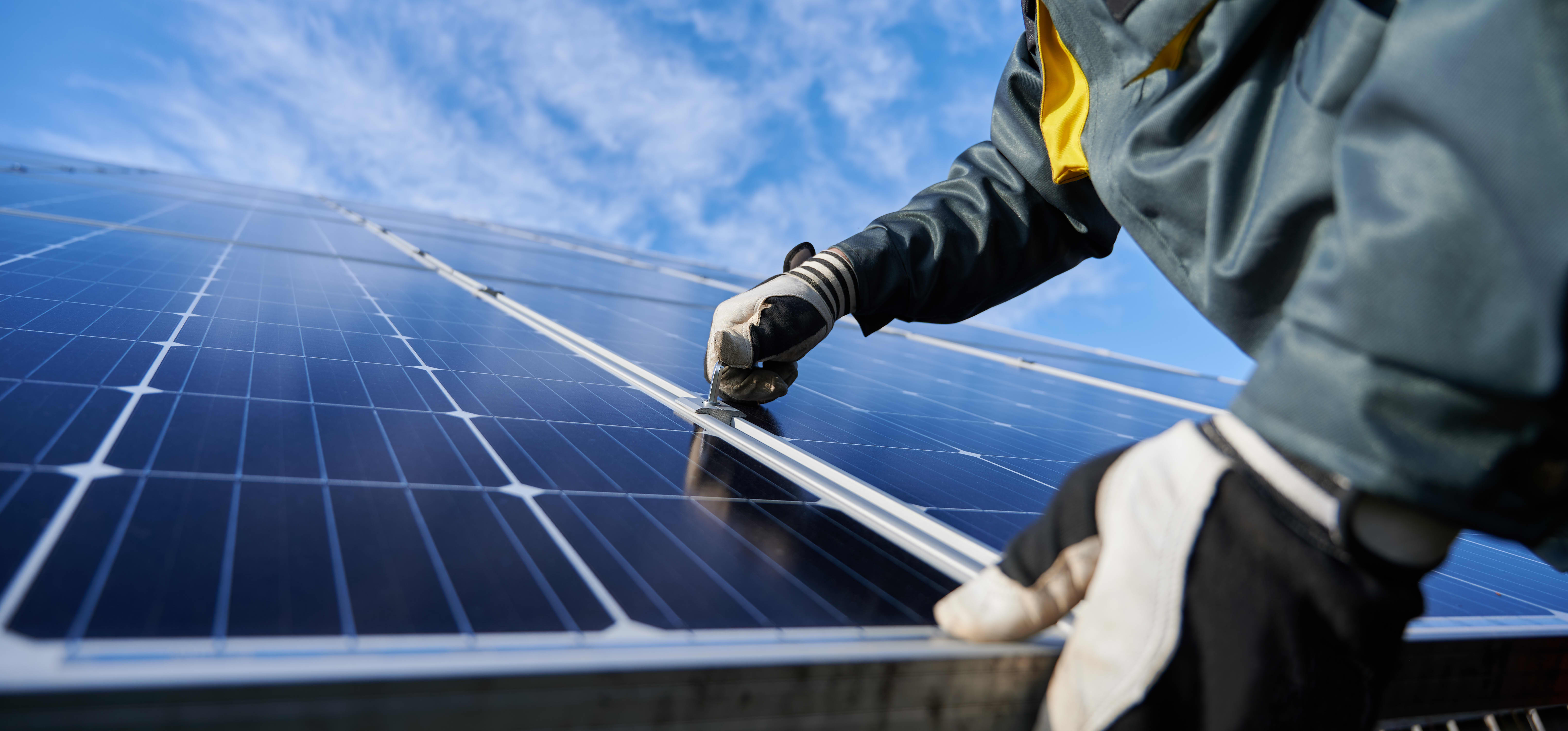 Nahaufnahme eines Arbeiters mit Handschuhen, der an einem installierten Solarmodul auf einem Dach arbeitet
