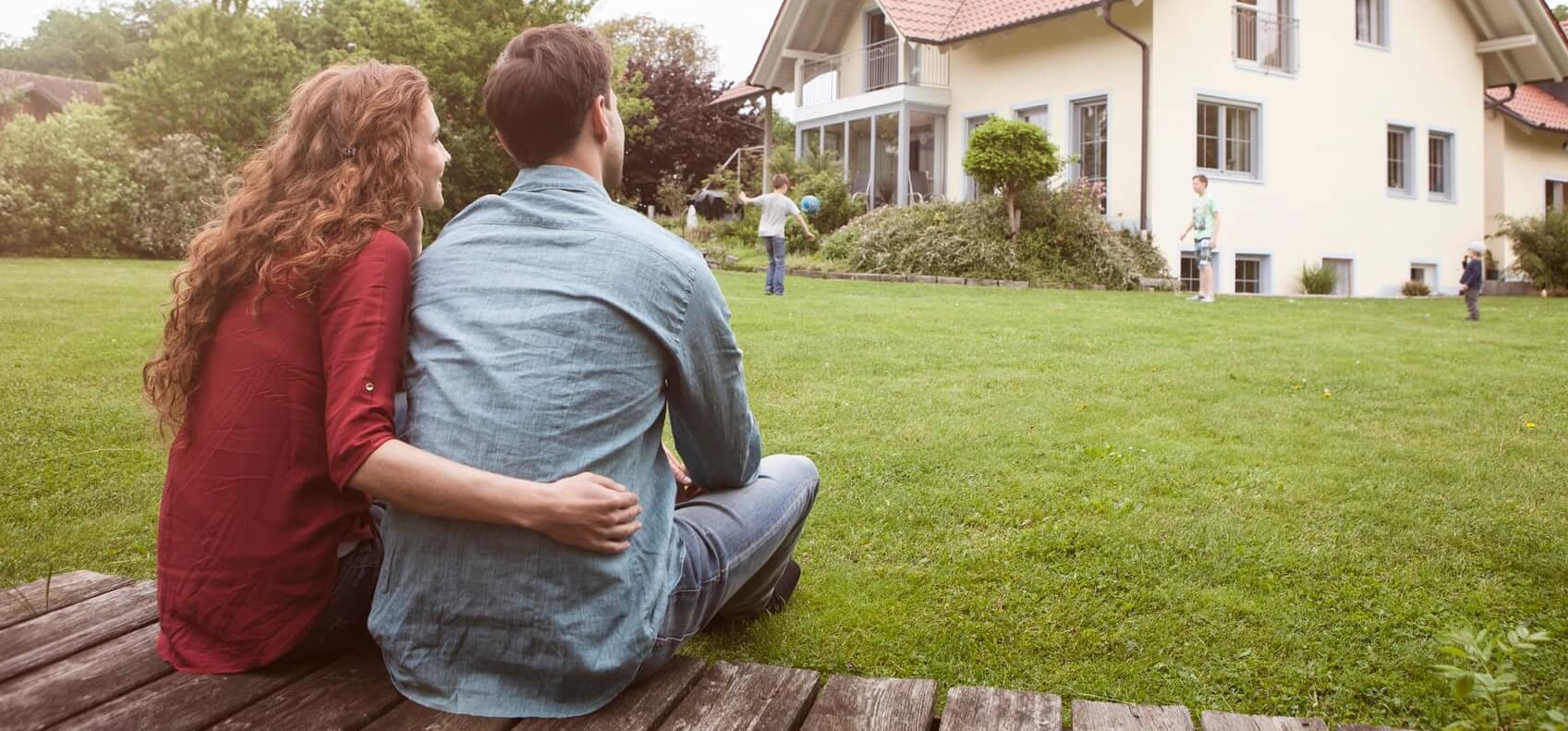 Junges Paar mit Kind im Garten vor einem Einfamilienhaus