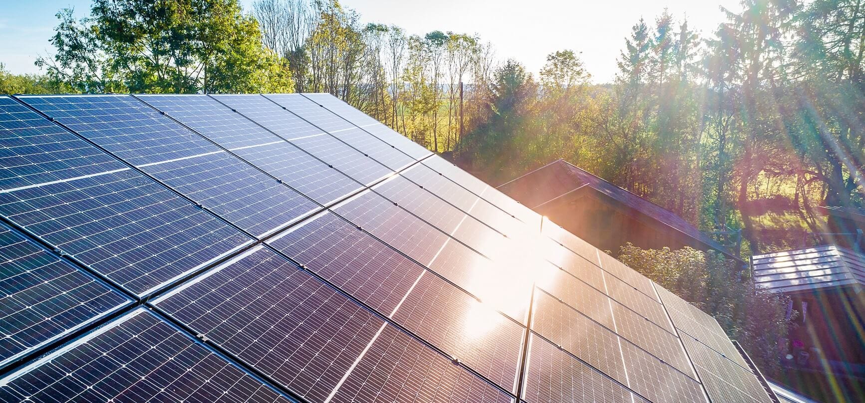 Solarpaneele und Sonnenlichtreflexionen auf dem Dach vor blauem Himmel und Bäumen im Hintergrund