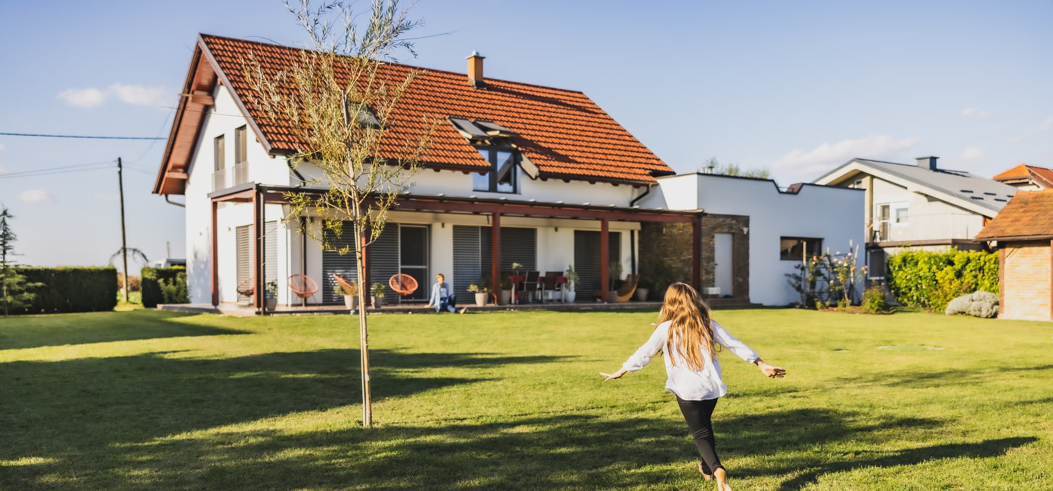 Mädchen rennt mit ausgebreiteten Armen durch den Garten aufs Wohnhaus zu