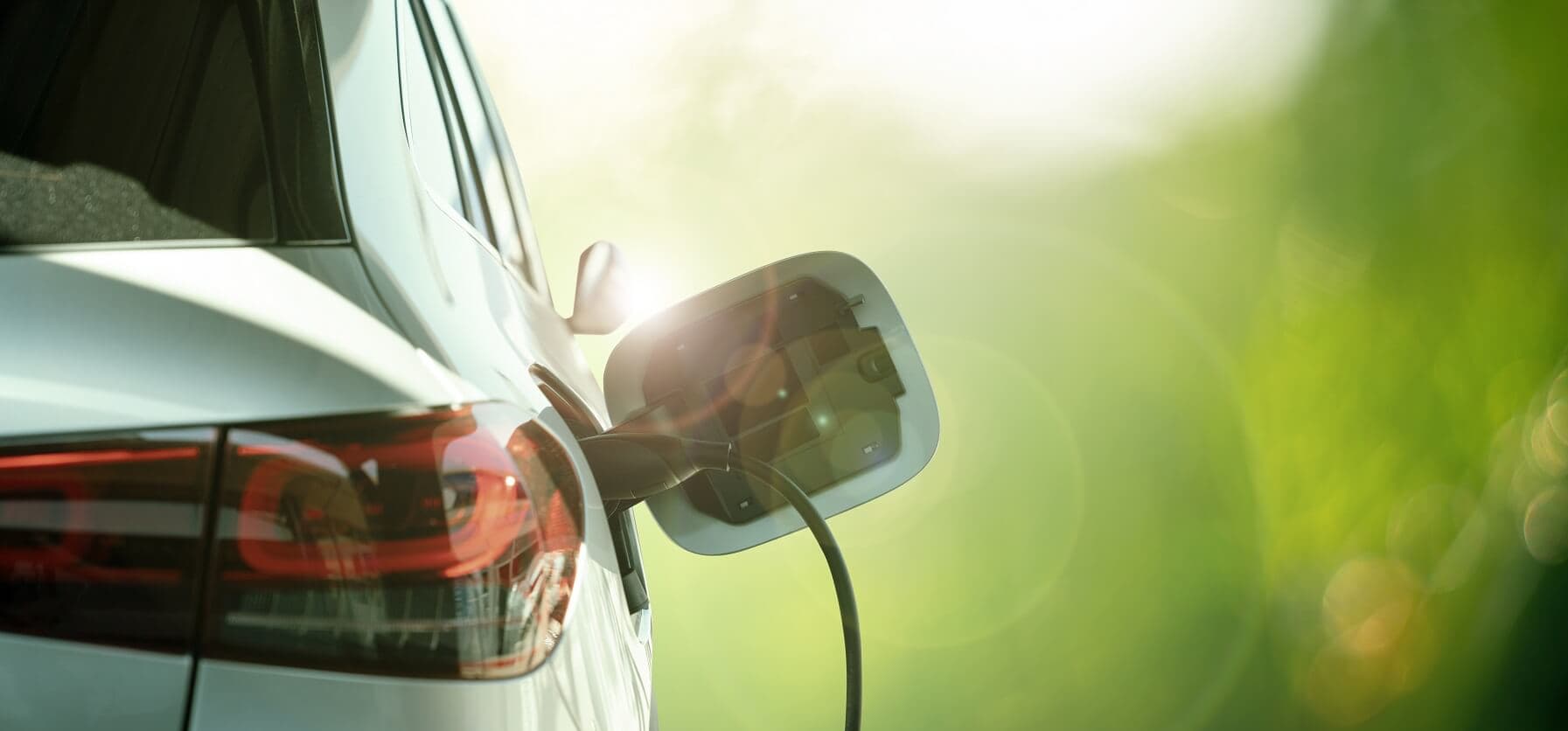 Weißes Elektroauto vor grünem Hintergrund wird geladen