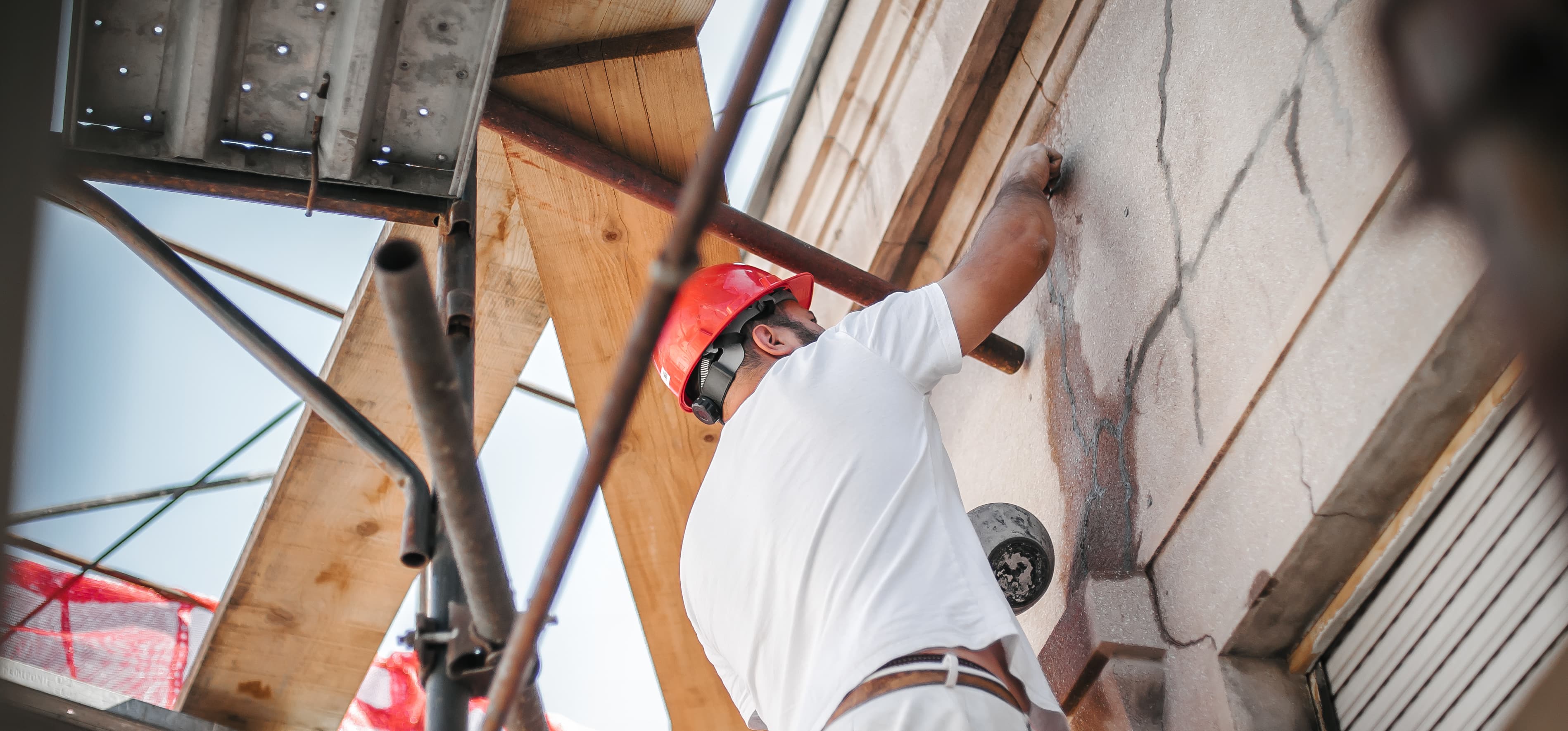 Ansicht eines Handwerkers mit weißer Kleidung und rotem Helm, der an einer Fassade arbeitet