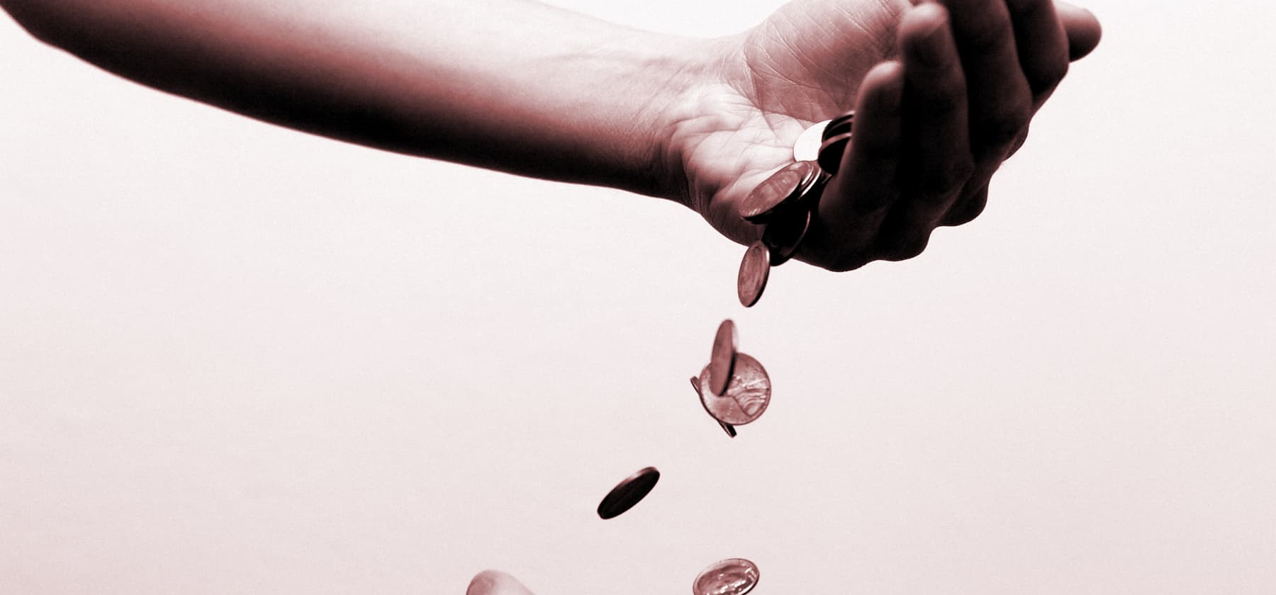Eine Hand vor rosa Hintergrund schüttet Münzen in eine Hand unter ihr