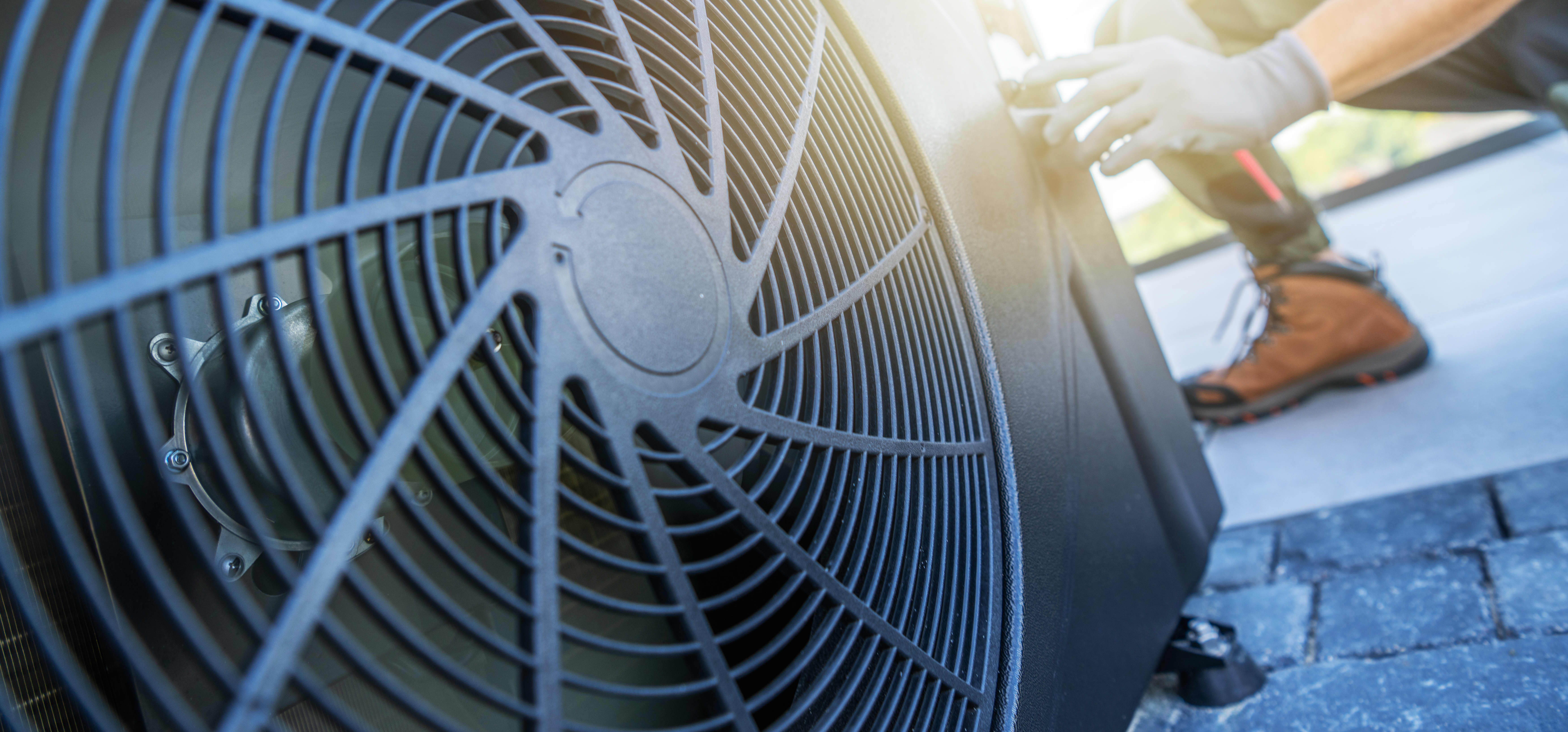 Ein Techniker führt Wartungsarbeiten an einer Klimaanlage auf einem Dach durch. Die Sonne scheint hell im Hintergrund