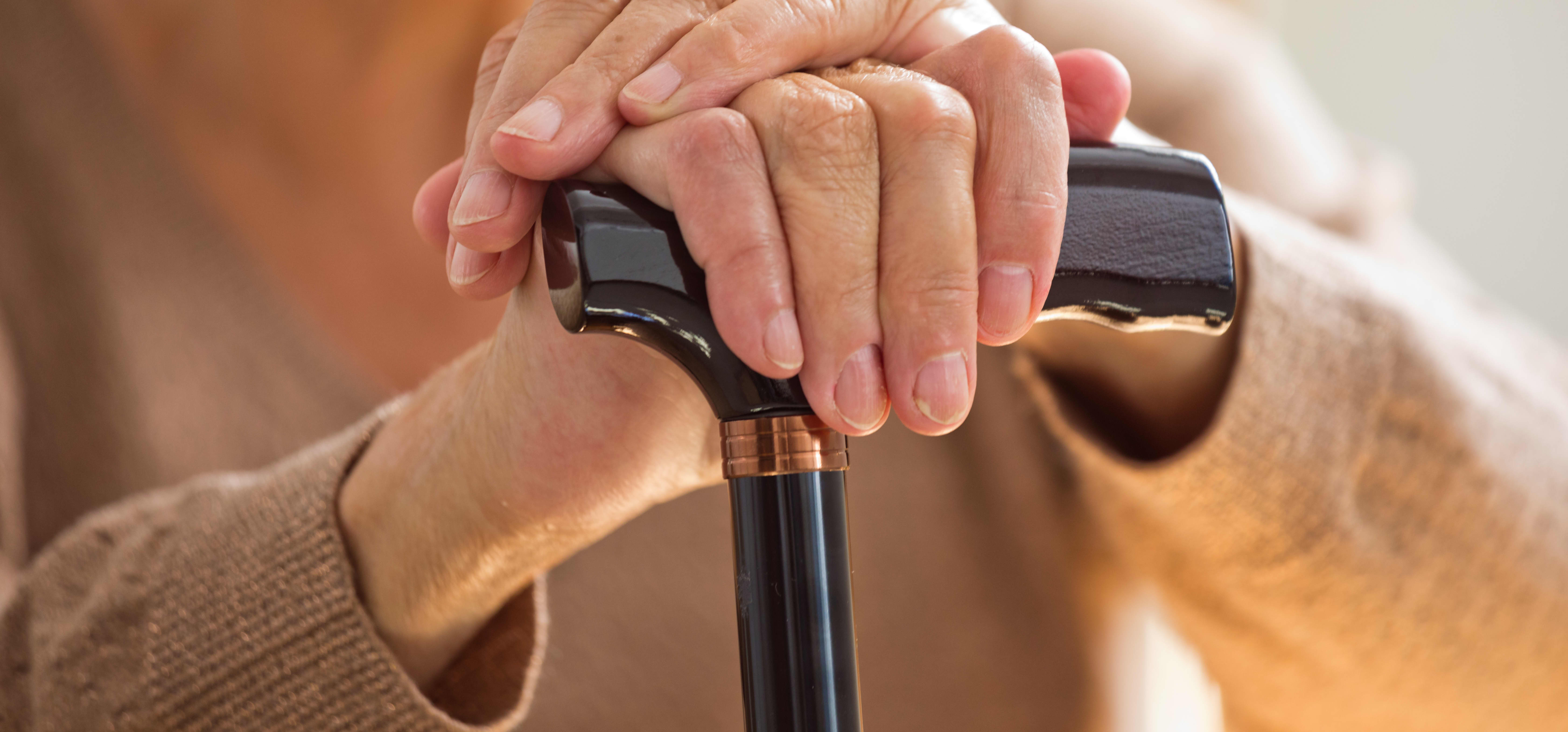 Seniorin hält einen Gehstock fest, der Fokus liegt auf ihren Händen