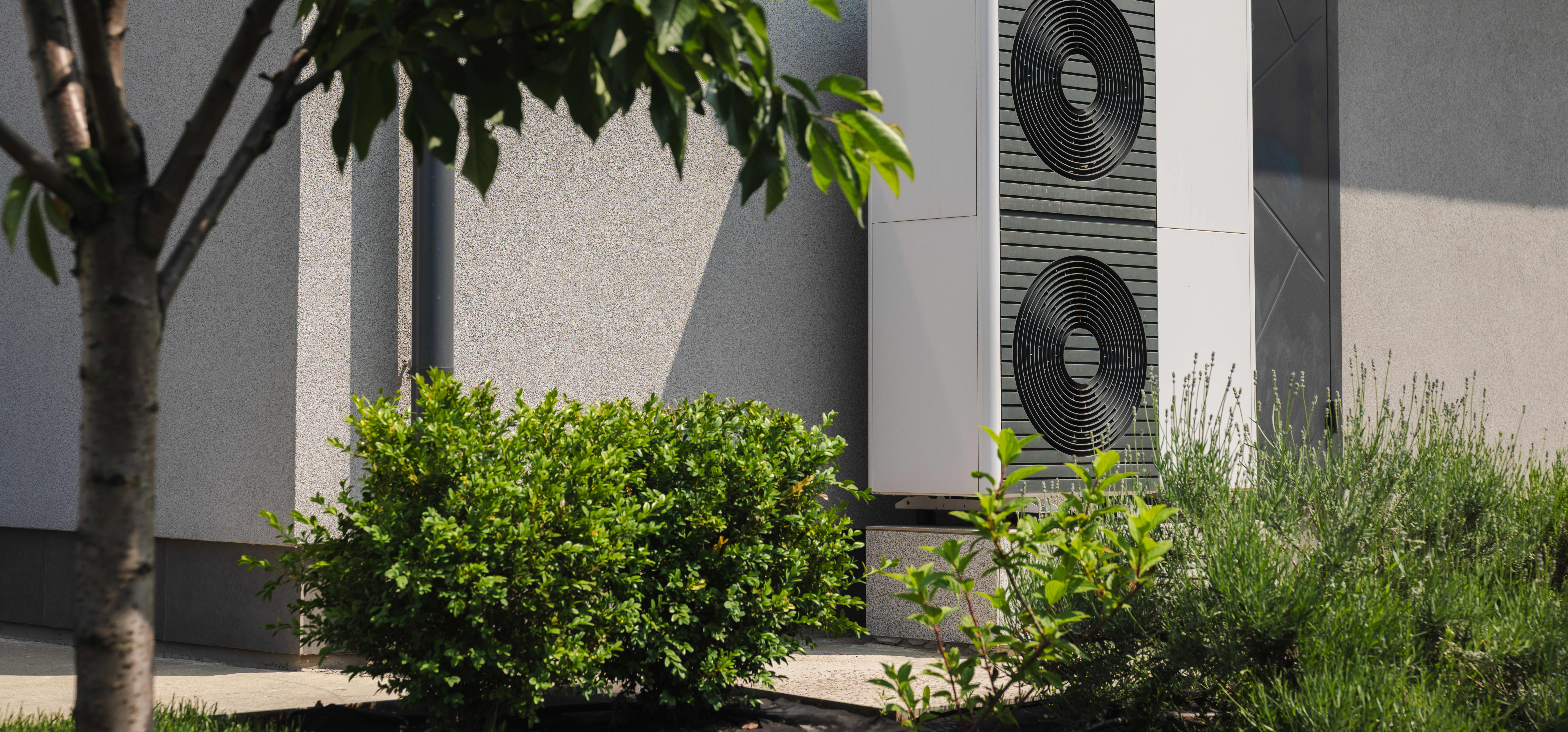 Moderne Wärmepumpen an der Fassade eines Wohnhauses mit grünem Garten