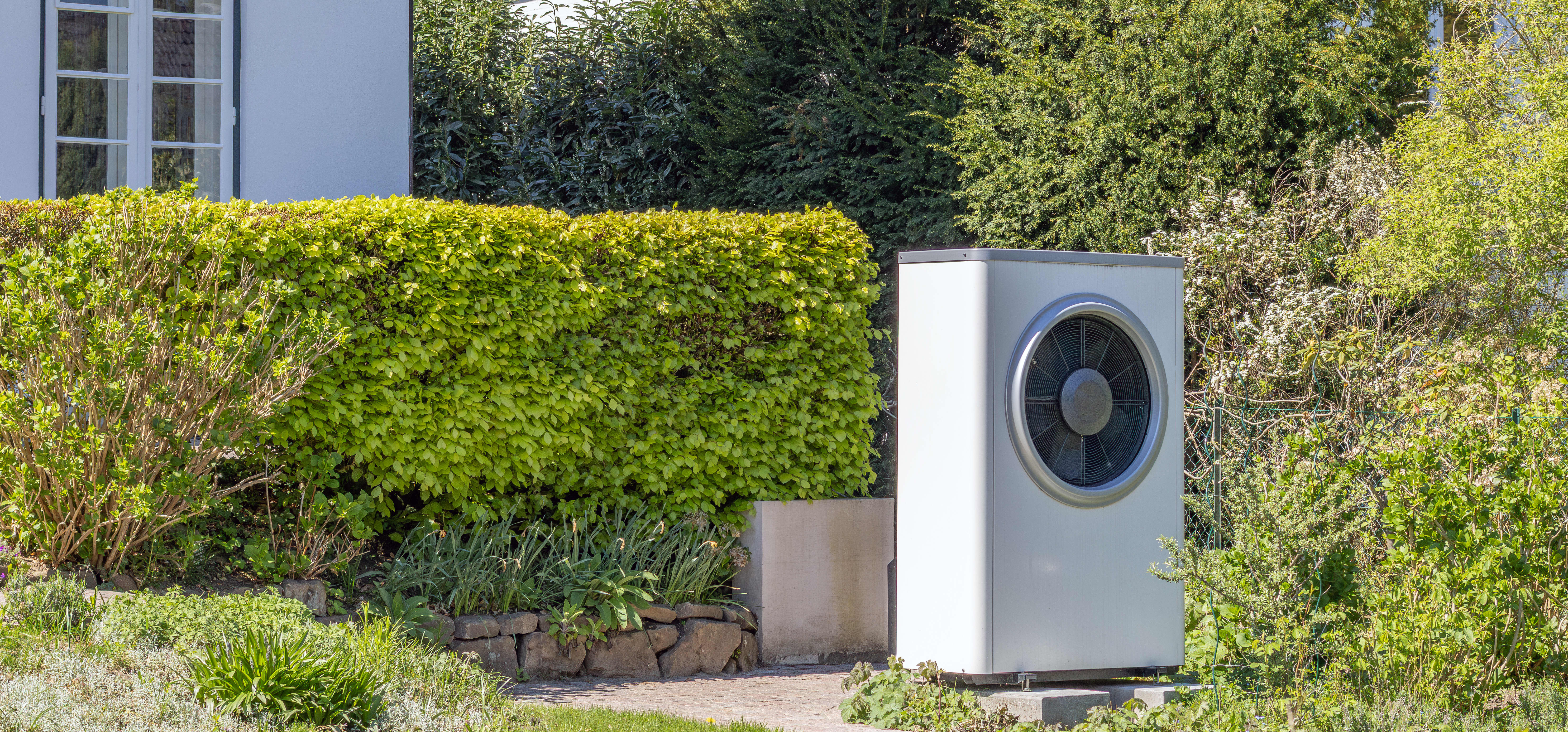 Wärmepumpe im Garten vor einem Haus im Grünen
